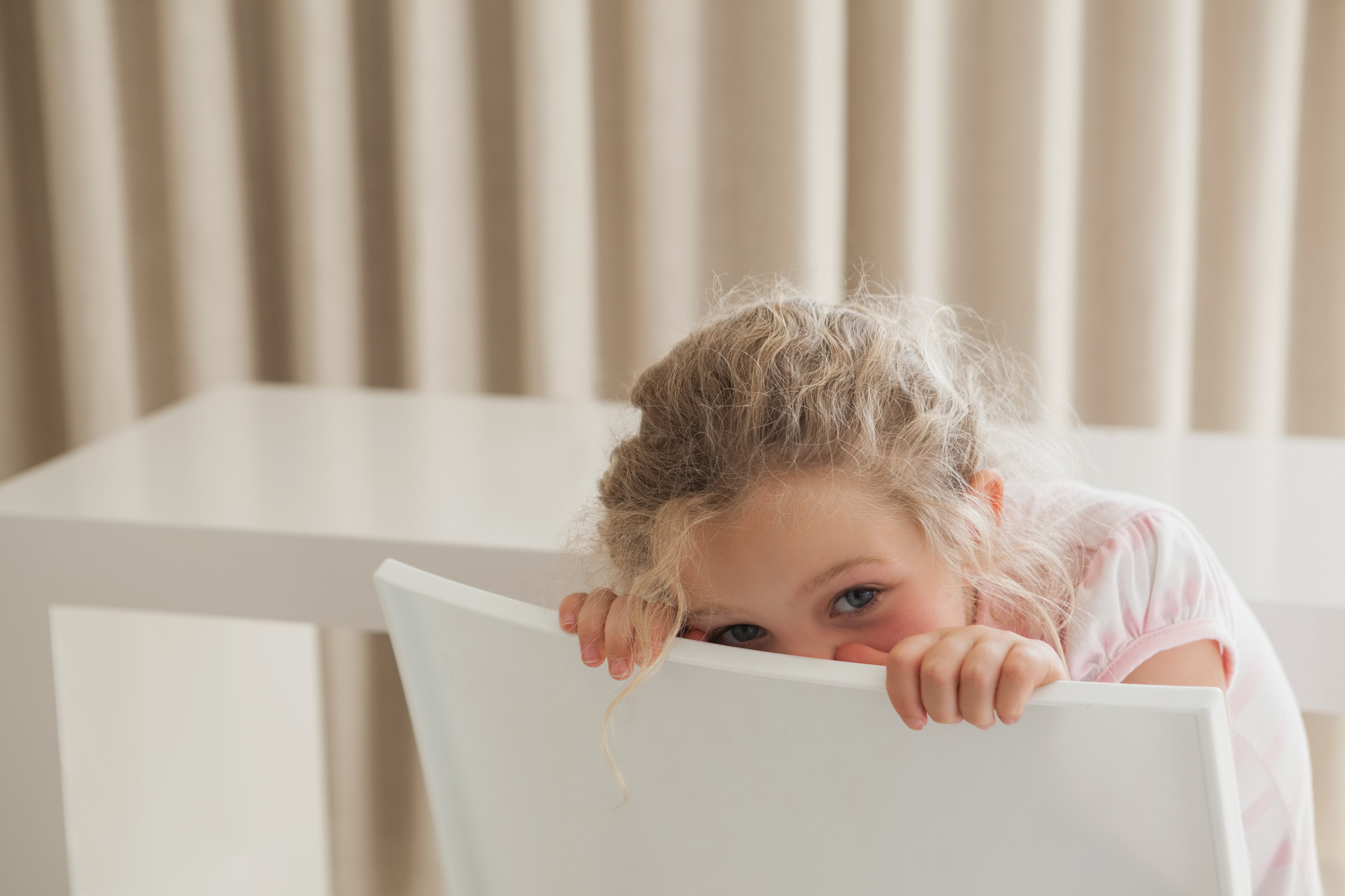 Little girl being shy and hiding behind chair while peeking over